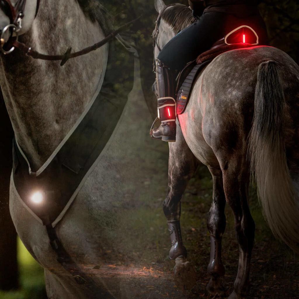 Frau auf Pferd im Dunkeln mit Leuchtmanschetten and Stiefel und Sattel